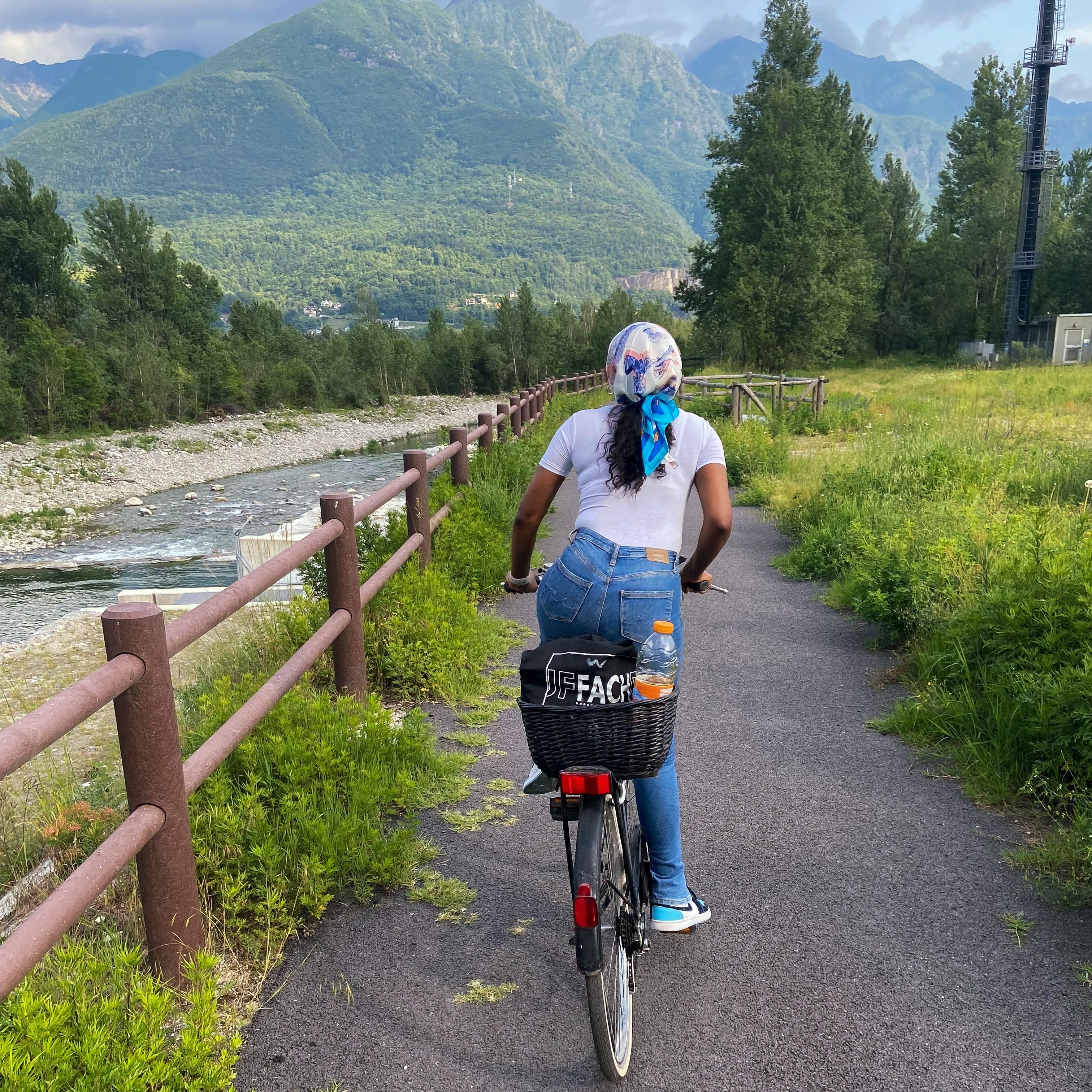 A person riding a bicycle along a scenic path, with mountains and greenery in the background.